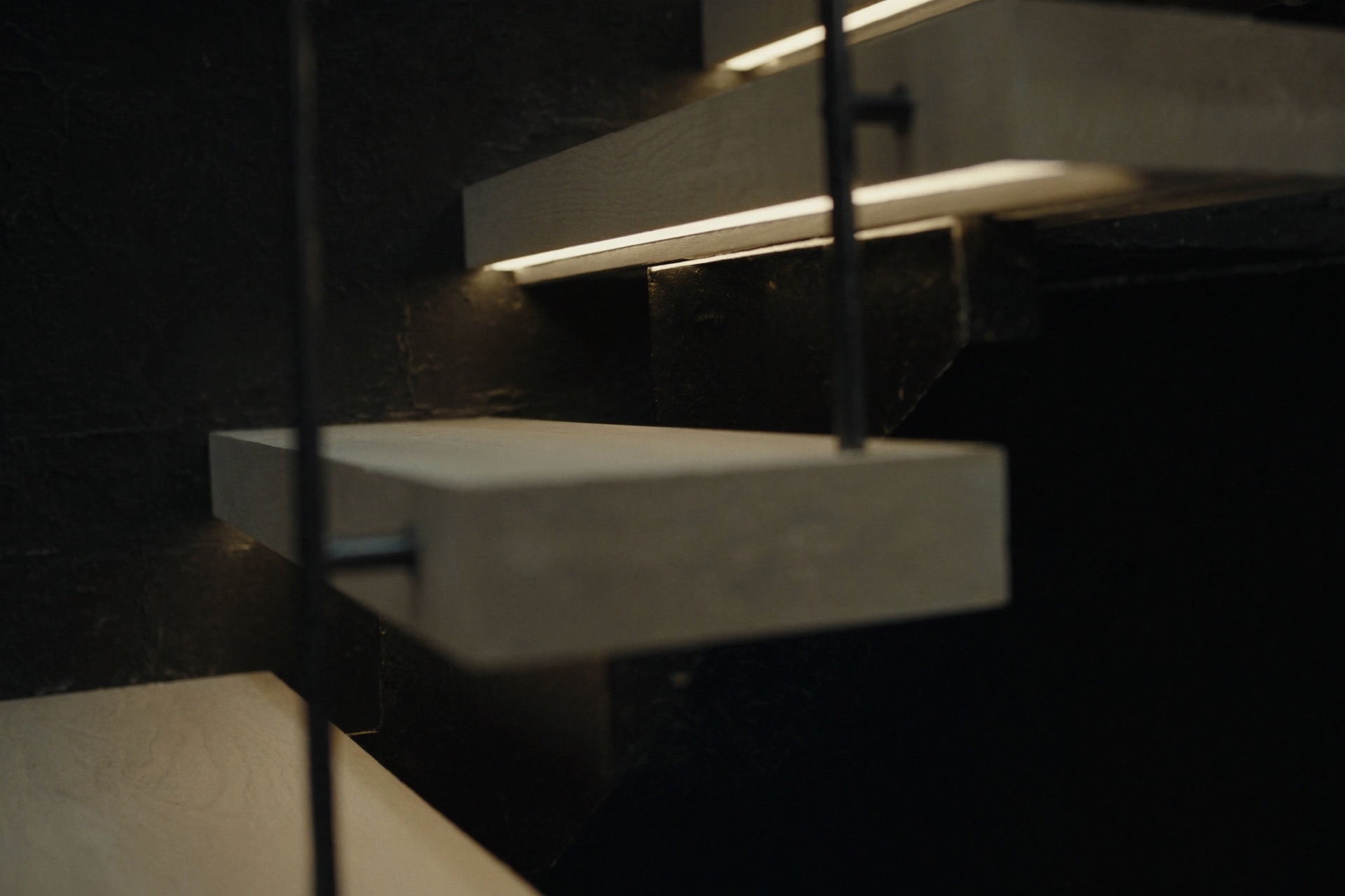 Close-up of the hand-bent blackened-steel stair, low warm light catching the rail