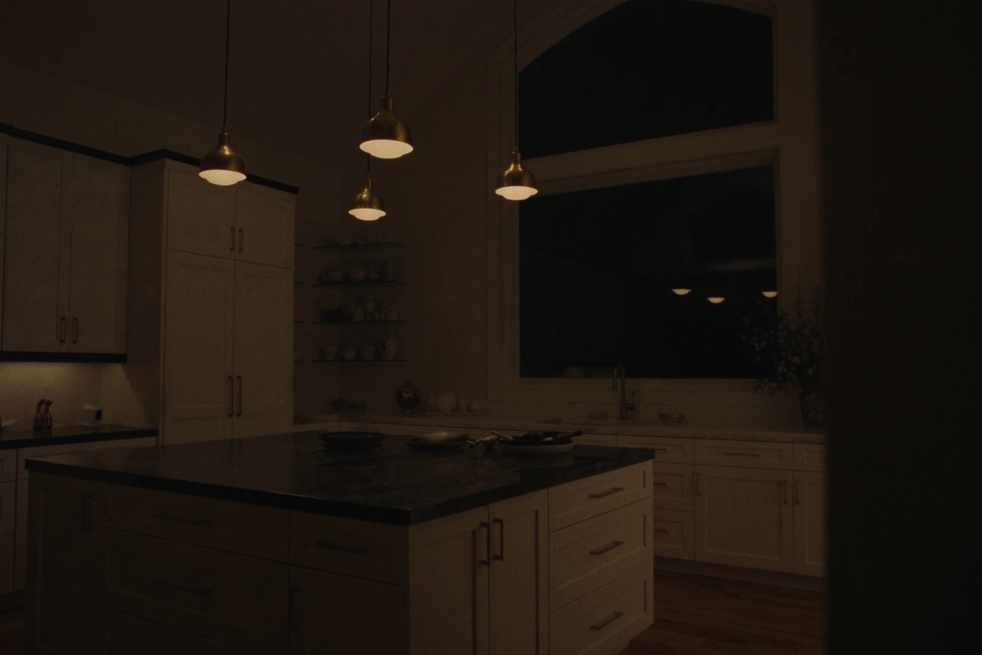 The Cedar Point kitchen at night — white-oak cabinetry and limestone under warm pendant light, lake darkness beyond the glass